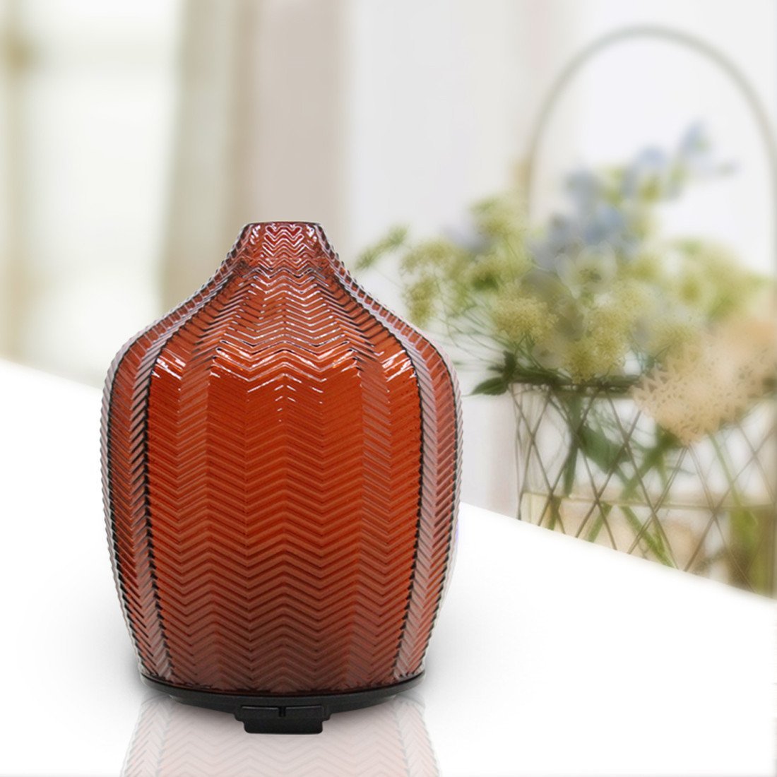Amber glass ultrasonic aroma diffuser on a white tabletop with soft natural lighting
